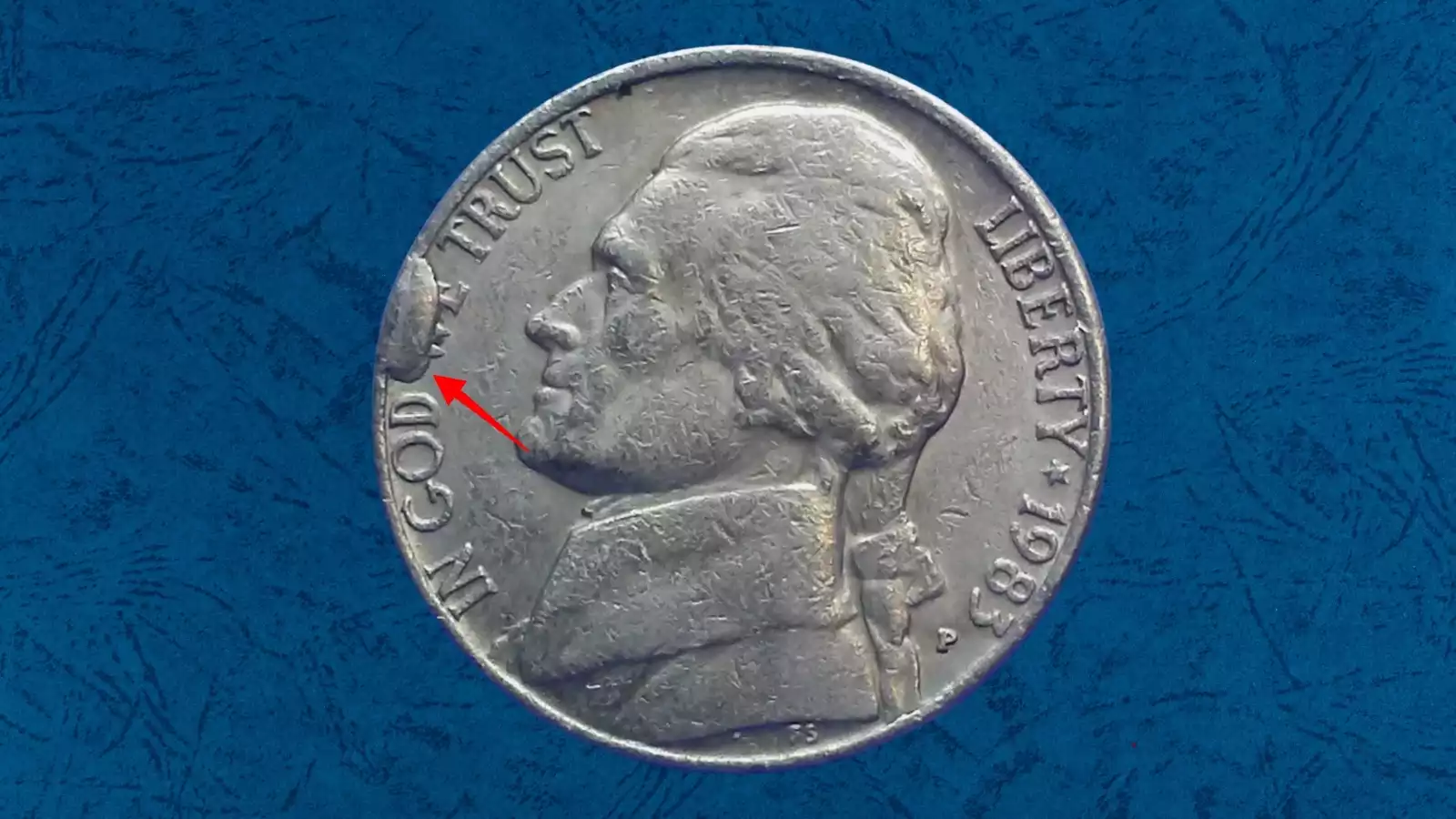 Close-up of a 1983 Jefferson nickel with a die cud error showing a raised featureless blob of metal near the coin's rim
